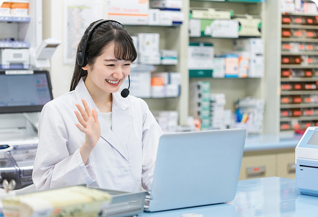 ヘッドセットを装着し笑顔で手を振る薬剤師